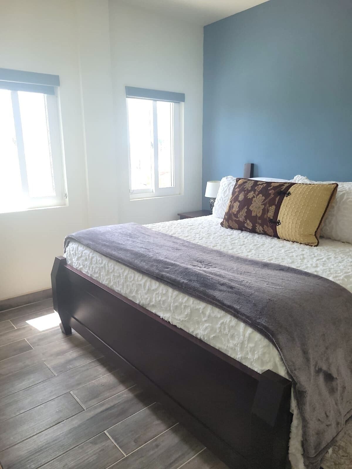 A bedroom with a bed, two windows, a nightstand, and a lamp.