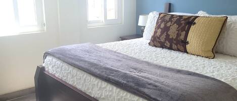 Une chambre à coucher avec un lit, deux fenêtres, une table de chevet et une lampe.