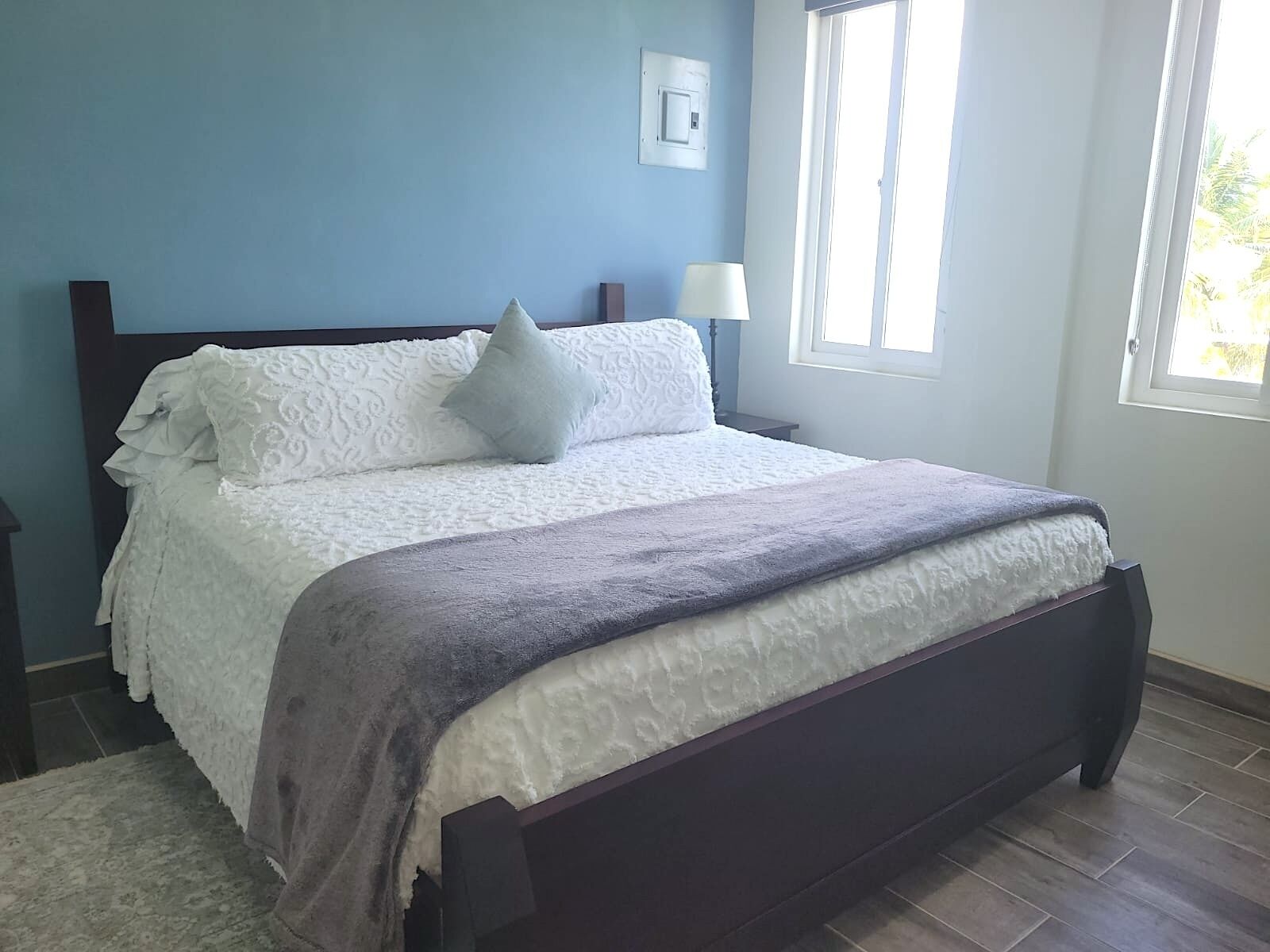 A neatly made bed with a white and gray blanket, a wooden headboard, and a nightstand with a lamp.