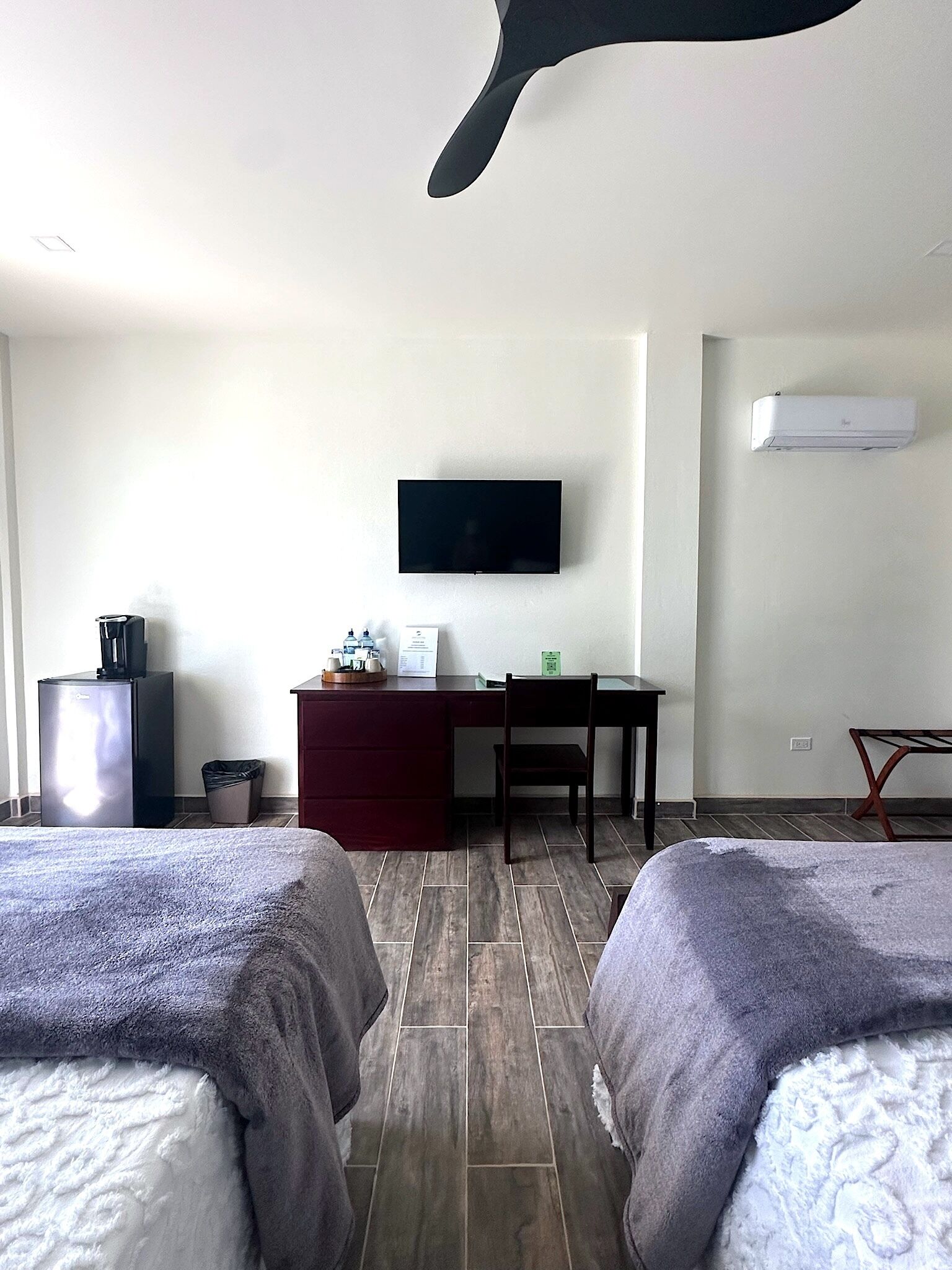 Habitación de hotel con dos camas, un escritorio, un televisor de pantalla plana, un refrigerador, un cesto de basura y un equipo de aire acondicionado.
