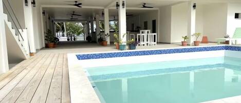 A swimming pool with a wooden deck and a covered area with ceiling fans.