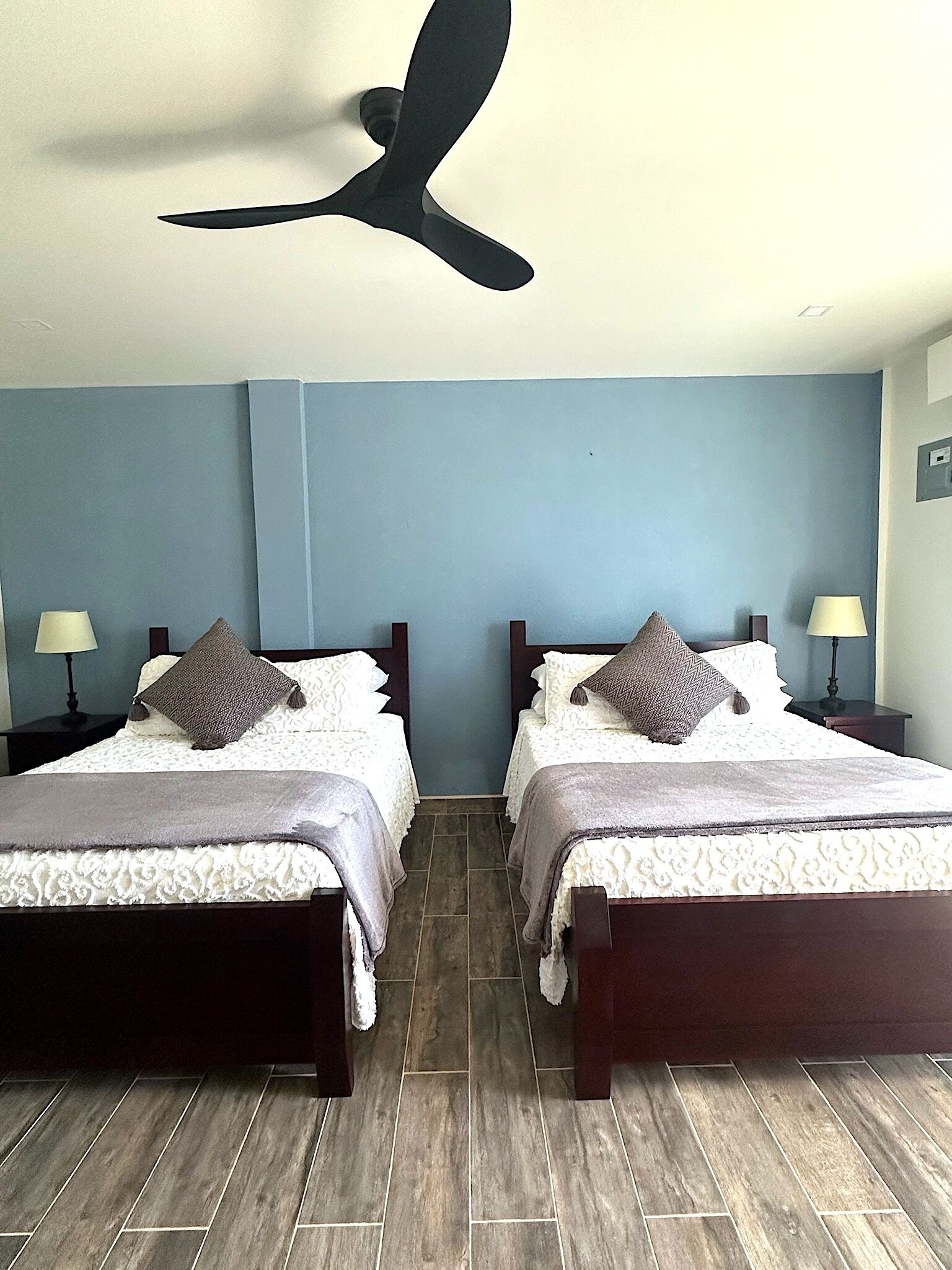A hotel room with two beds, a ceiling fan, and a blue wall.