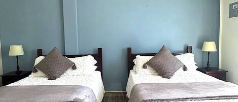 Habitación de hotel con dos camas, ventilador de techo y pared azul.