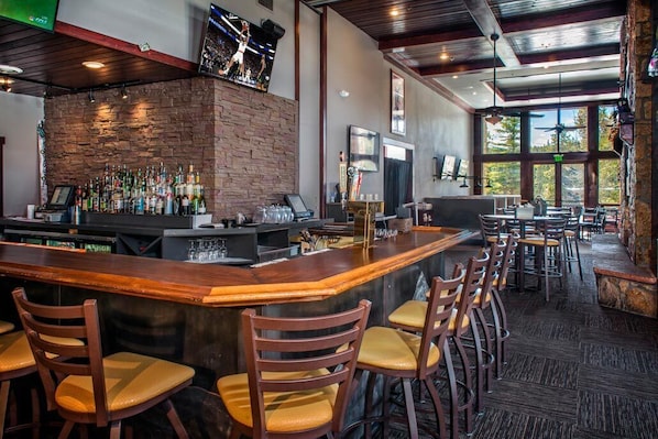 A bar area with a brick wall, wooden bar counter, and multiple bar stools.