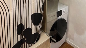 A bathroom with a striped shower curtain, a glass shower enclosure, a white washing machine, and a shelf with folded towels. - F3 with terrace and secure parking (Châteaugay)