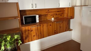 A kitchen with wooden cabinets, a microwave, a small plant, and a refrigerator. - F3 with terrace and secure parking (Châteaugay)