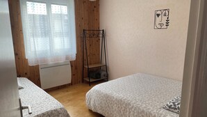 A bedroom with two beds, a radiator, a wooden wardrobe, and a window with sheer curtains. - F3 with terrace and secure parking (Châteaugay)