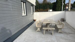 A concrete patio with a table and benches, a grey building wall, and a green fence in the background. - F3 with terrace and secure parking (Châteaugay)