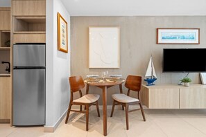 A modern kitchen with a built-in refrigerator, wooden cabinets, a dining table with chairs, a flat-screen TV, and framed artwork on the walls.