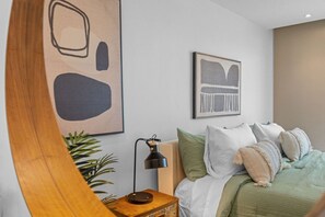 Una camera da letto con un letto, cuscini, un comodino, una lampada e due opere d'arte appese alle pareti.