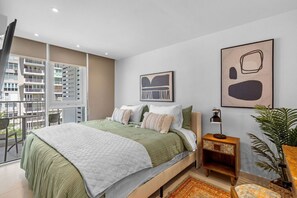 A modern bedroom with a large bed, a nightstand, a lamp, and a potted plant.