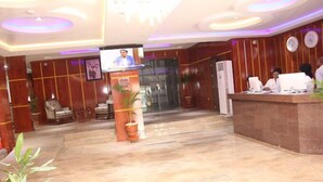 A hotel lobby with a reception desk, a television screen, and a seating area. - Asabana Suites and Hotels Ltd (Asaba)
