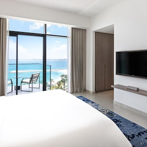 Habitación de hotel con una cama grande, un televisor montado en la pared y un balcón con vista al mar.
