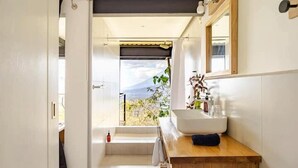 A bathroom with a large window, a wooden vanity, a white sink, and a mirror.