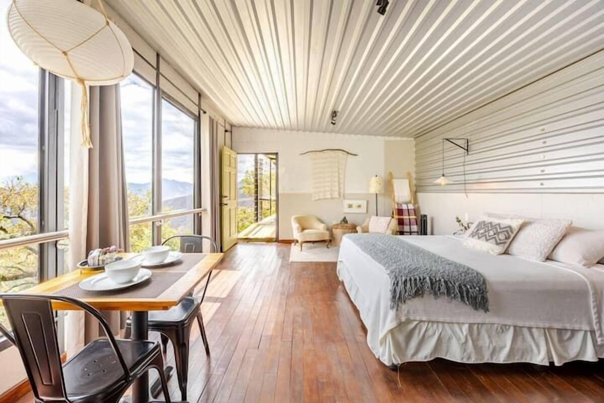 Een slaapkamer met een bed, een tafel met stoelen, een raam en uitzicht op de omgeving.