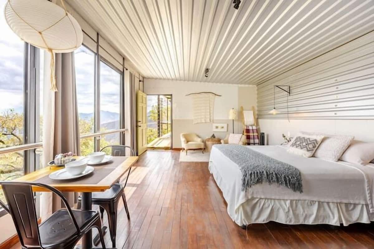 A bedroom with a bed, a table with chairs, a window, and a view of the outdoors.
