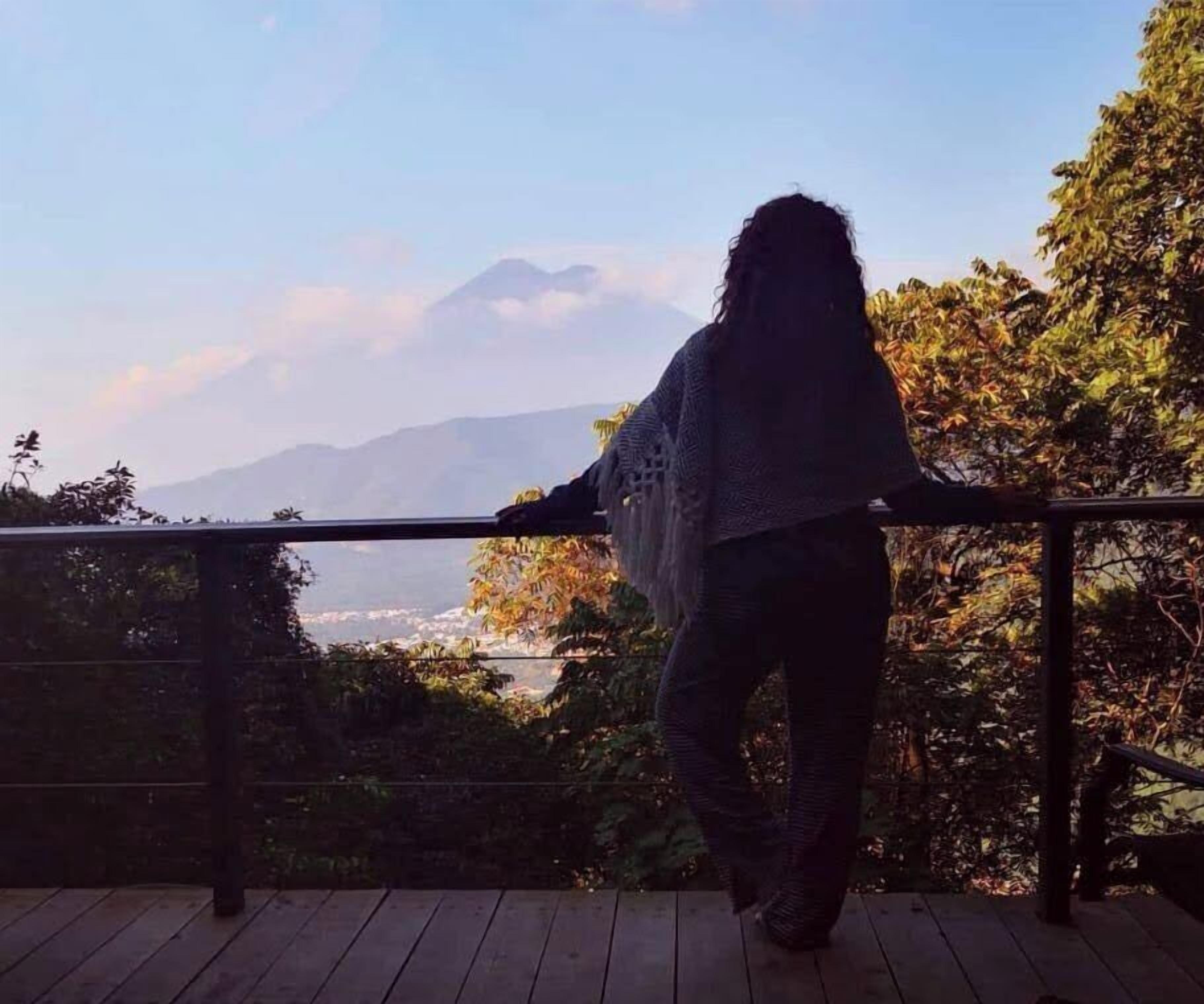 A person standing on a wooden deck overlooking a mountainous landscape.