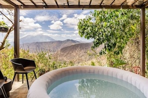 A hot tub with a mountain view, a chair, and a table. - Finca El Tambor (Antigua Guatemala)