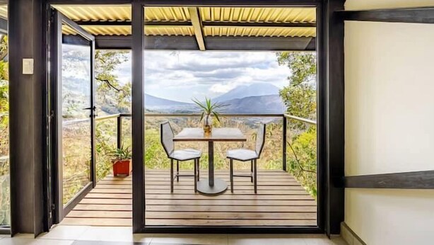 A balcony with a table and chairs, a potted plant, and a view of mountains.