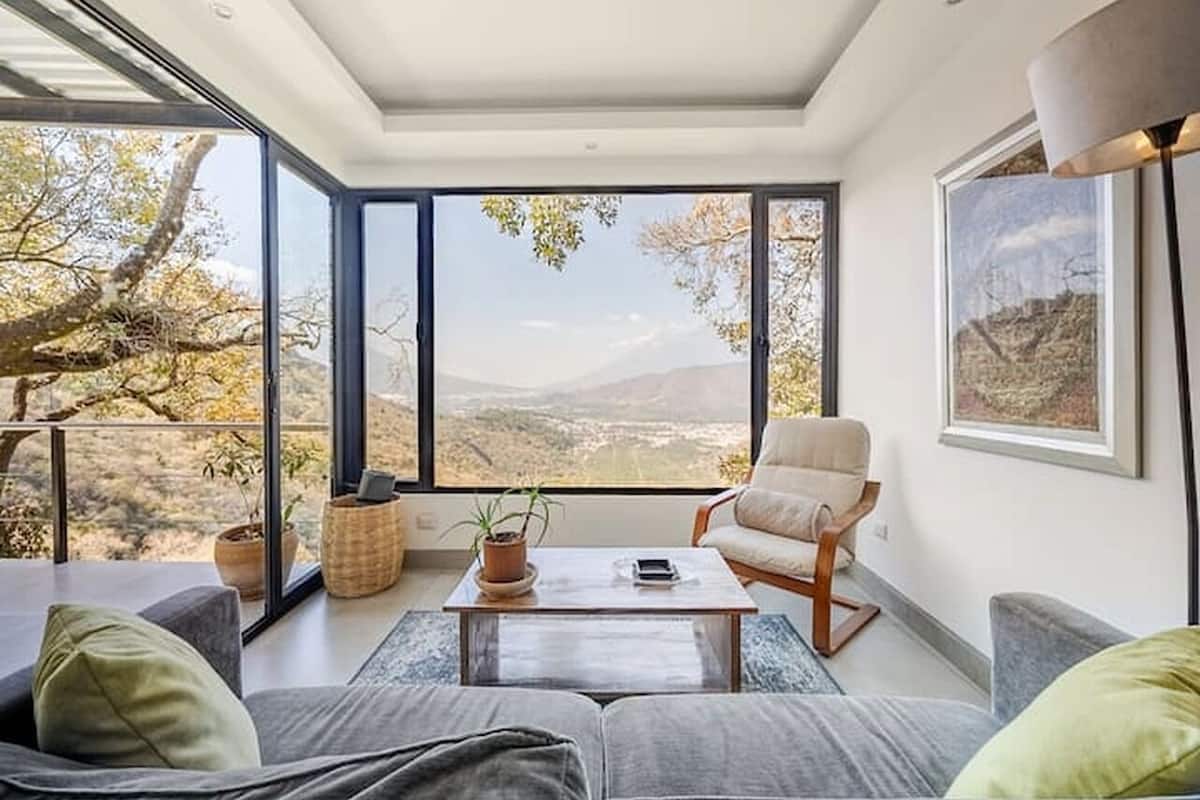 A modern living room with large windows, a sofa, a chair, and a coffee table.