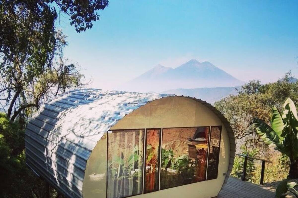 Een modern, gebogen gebouw met grote ramen, een houten terras en uitzicht op een bergketen.