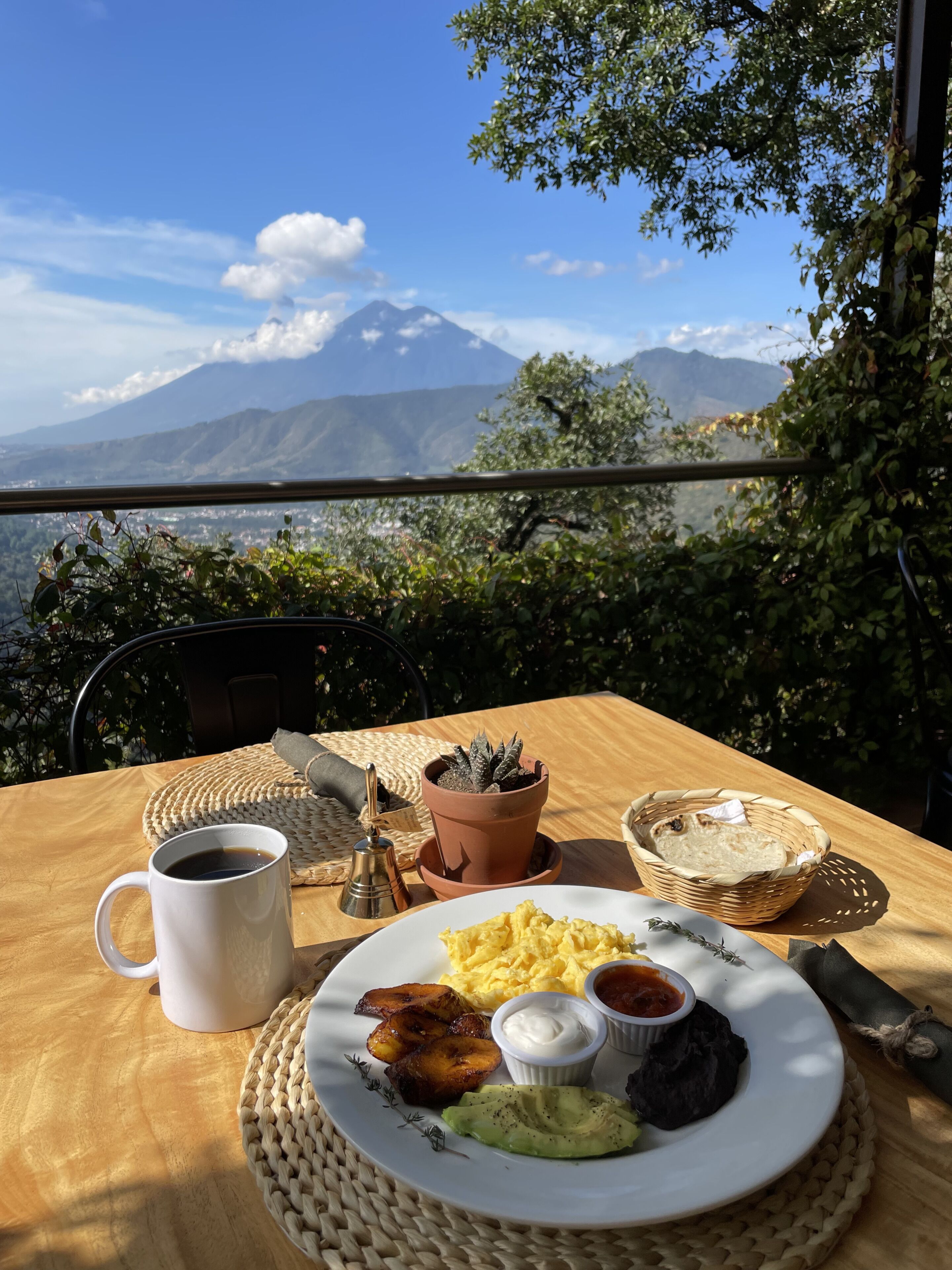 Ett bord med frukostmat, en krukväxt och utsikt över bergen.