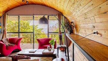 Una habitación acogedora con techo de madera curvada, ventanas amplias, sillas rojas, una mesa de centro y una planta.