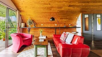 A modern living room with a wooden ceiling, a red sofa, a red chair, a wooden coffee table, and a floor lamp.