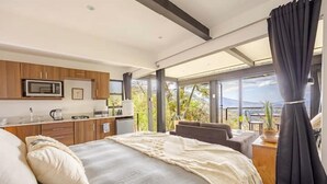 A bedroom with a large bed, a kitchenette, and a balcony with a view.