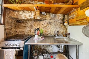 Cocina compacta con pared de piedra, estufa a gas, lavamanos y diversos utensilios.