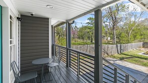 Eine überdachte Veranda mit Tisch und Stühlen, Blick auf den Garten und ein Holzzaun.