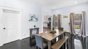 Ein Essbereich mit Holztisch, Stühlen, einer Bank, einem kleinen Tisch mit Blumenvase und einer Küche im Hintergrund.