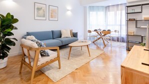 Uma sala de estar moderna com um sofá azul, cadeiras de madeira, uma pequena mesa redonda e uma estante.