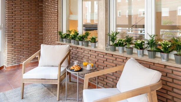 Uma área de estar aconchegante, com duas poltronas brancas acolchoadas e uma pequena mesa com croissants e suco de laranja.