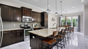 A modern kitchen with dark wood cabinets, stainless steel appliances, granite countertops, and a central island with bar stools. - 948B - 4BR $700+ in freebies incl golf, Pool (Miramar Beach)