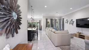 A modern living room with a sectional sofa, a dining area with a glass-top table, and a large TV on the wall. - 948B - 4BR $700+ in freebies incl golf, Pool (Miramar Beach)
