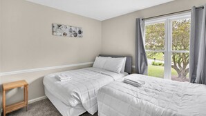 A bedroom with two beds, a small table, a ceiling light, and a window with curtains. - Family Friendly in Forestdale  (Birmingham)
