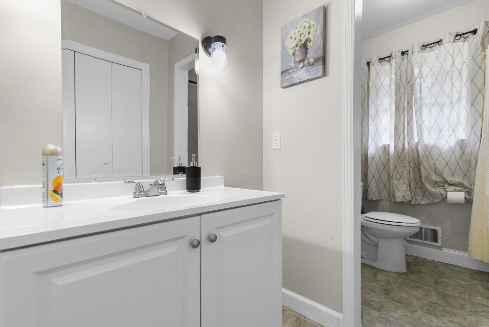 A bathroom with a white vanity, a mirror, a light fixture, a toilet, and a shower curtain.