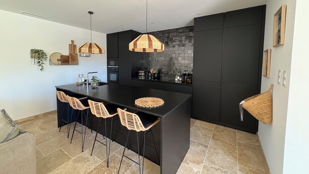 Une cuisine moderne dotée d’un îlot central, de meubles de rangement noirs et de luminaires au design tressé.