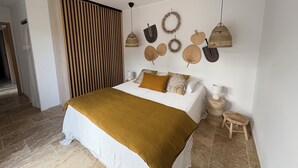 Une chambre avec un lit, une cloison en lattes de bois, un mur orné de motifs tissés et un petit tabouret en bois.