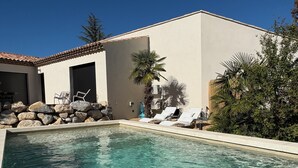 Une piscine avec des chaises longues, un mur en pierre et un bâtiment doté d’un toit en tuiles.