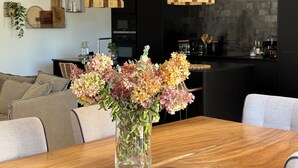 Une cuisine moderne avec des meubles de couleur sombre, une table à manger en bois et un vase rempli de fleurs.