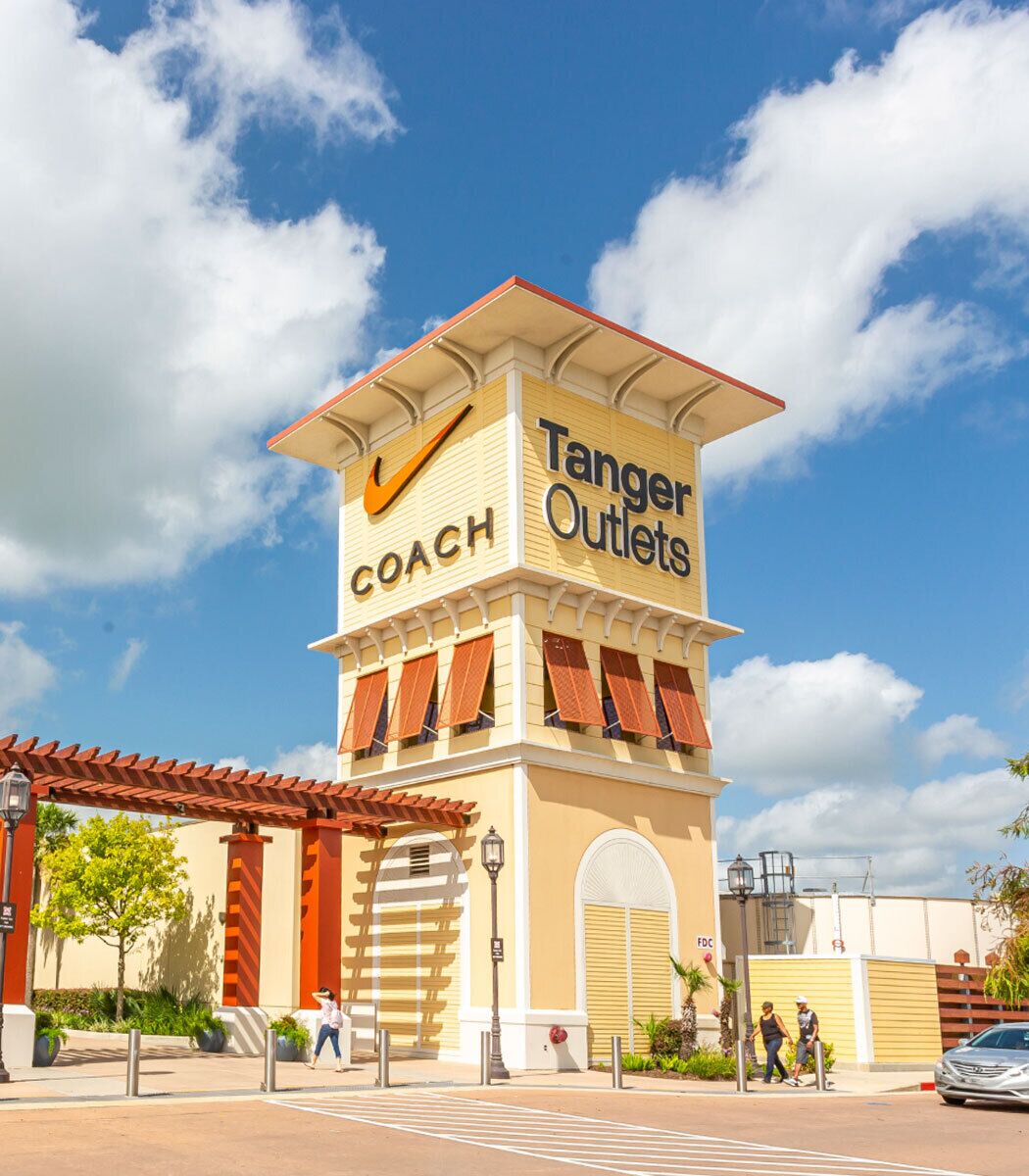A building with a sign reading "Tanger Outlets" and "Coach" on the facade.
