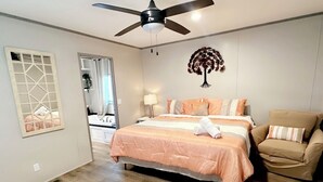 A bedroom with a bed, a chair, a ceiling fan, a wall decoration, and a window with a view. - Cozy 2BED 2BATH Home with central AC (Bacliff)