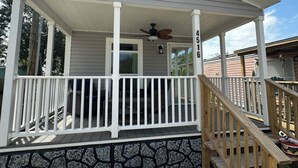 A covered porch with a wooden railing, a ceiling fan, and a stone foundation. - Cozy 2BED 2BATH Home with central AC (Bacliff)