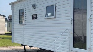 A white mobile home with a small window and a door. - 3 Bedroom Caravan to Hire (Abergele)