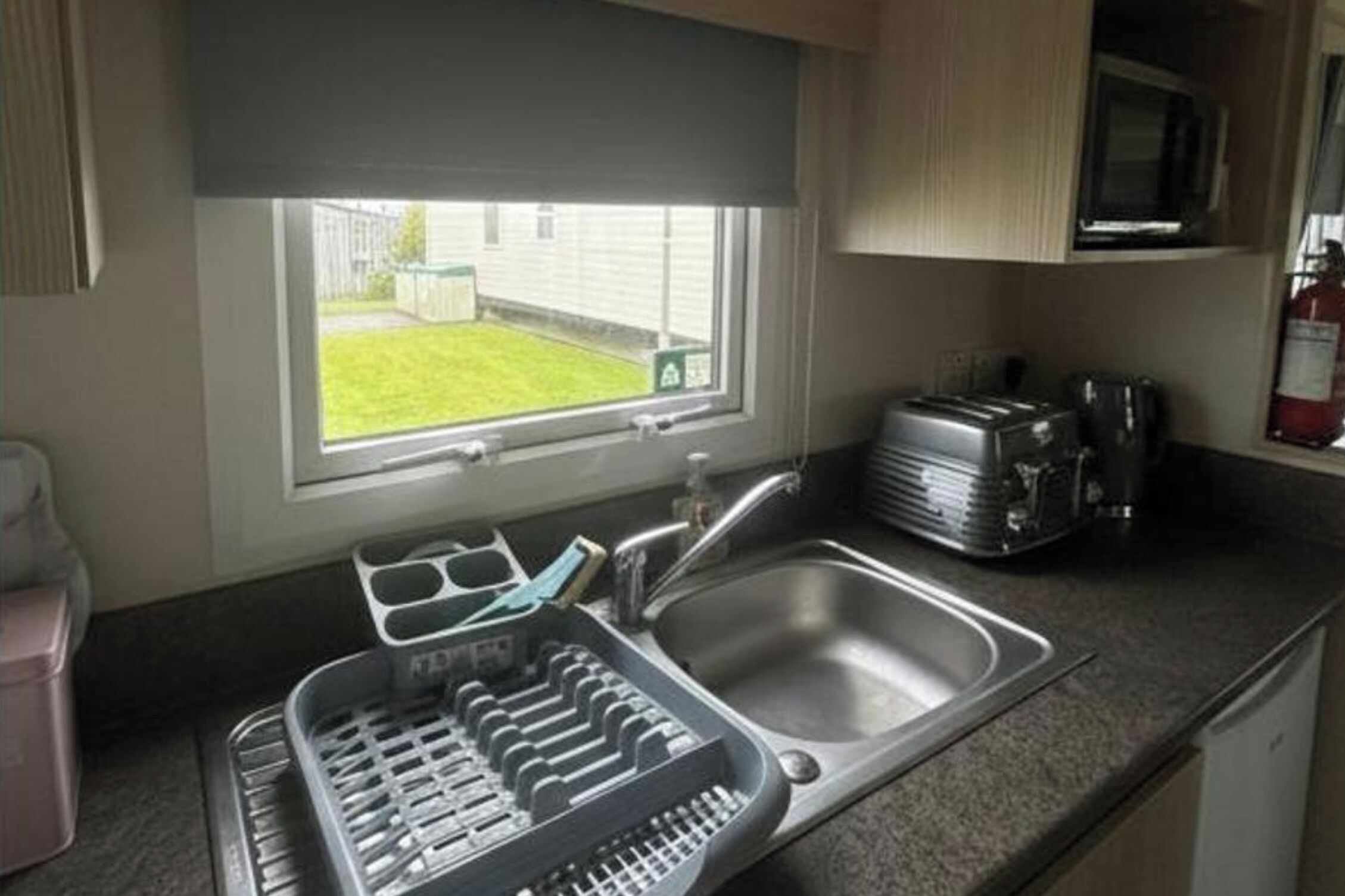 A compact kitchen with a window, a sink, a toaster, and a dish rack.