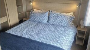 A bedroom with a bed, bedside tables, and a built-in wardrobe. - 3 Bedroom Caravan to Hire (Abergele)