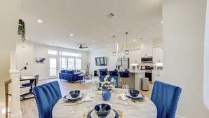 Un'area pranzo moderna con un tavolo rotondo apparecchiato per sei persone, sedie imbottite blu e una cucina sullo sfondo.