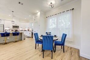 A modern kitchen with white cabinets, a central island, and a dining area with blue chairs and a round table. - Modern Cozy Home with King Bed (Houston)